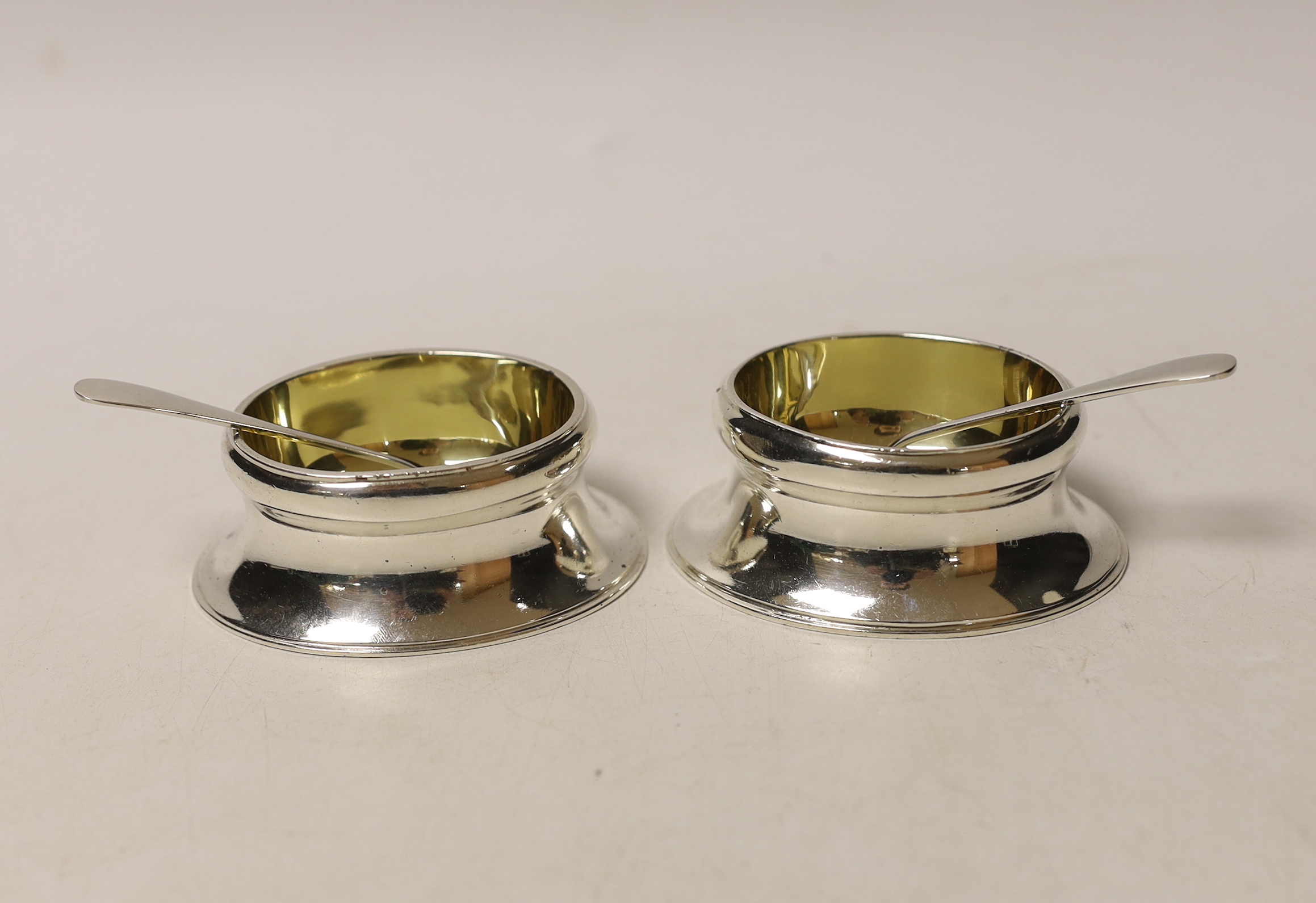 A boxed pair of George VI Britannia standard silver oval salts, Peter Guile Ltd, London, 1939, 8cm and a pair of late associated silver spoons.